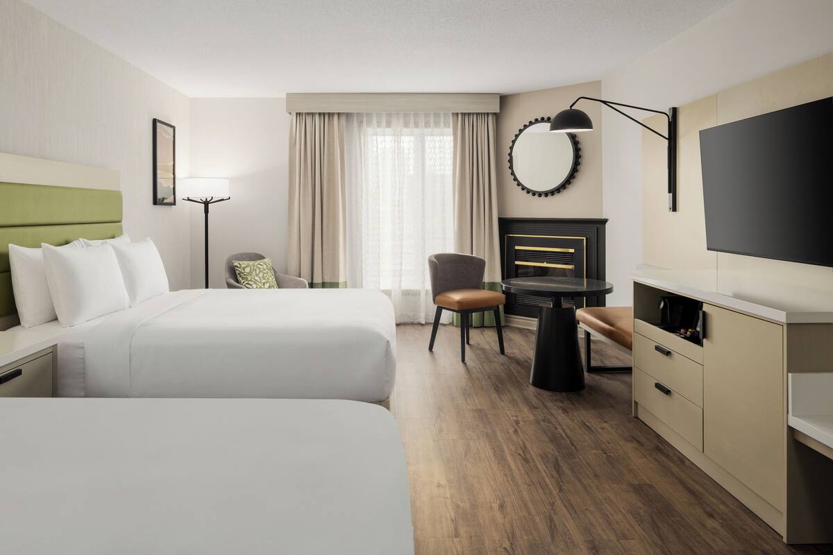 Une chambre d’hôtel avec deux lits, un bureau, une chaise, une télévision et une cheminée.