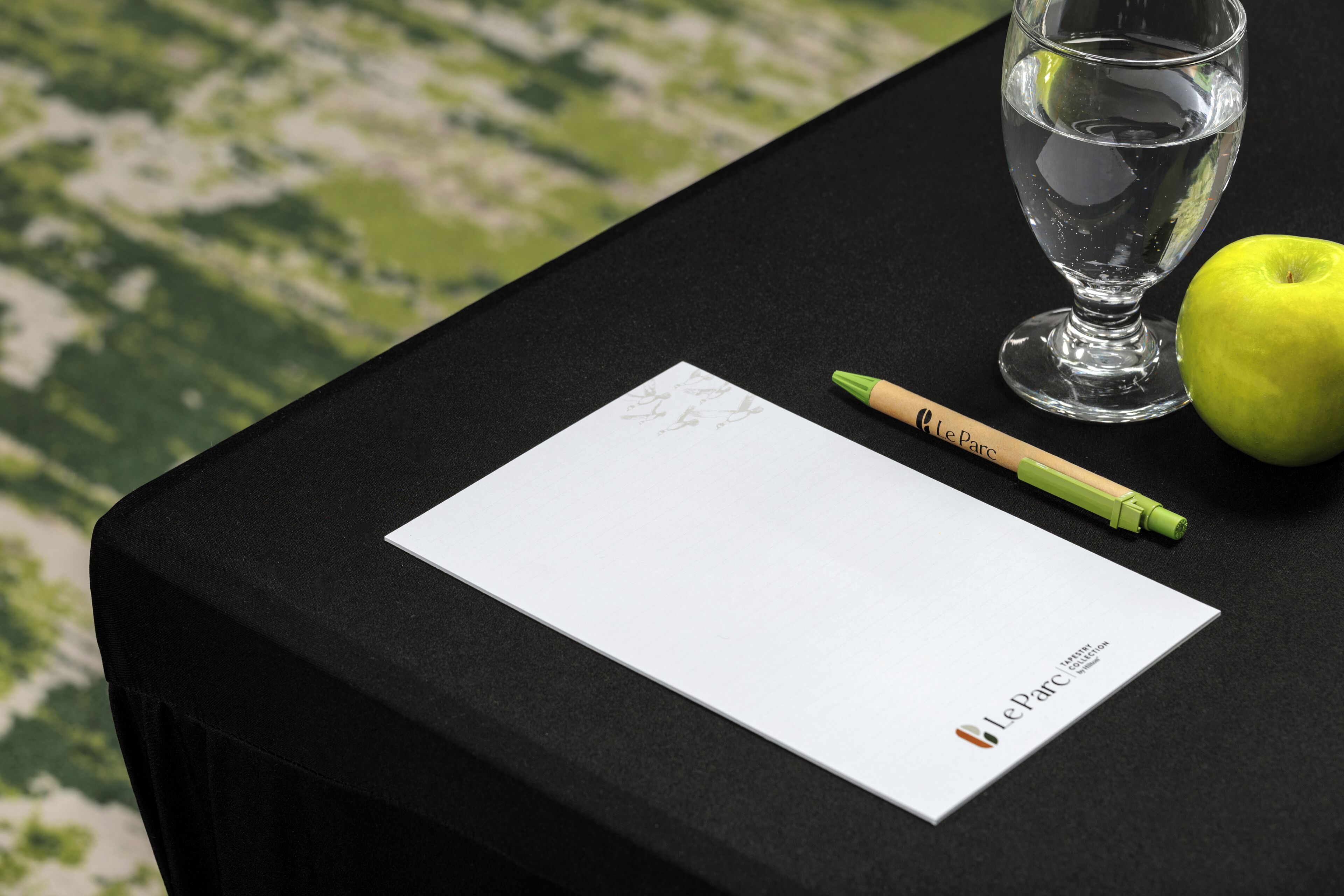 Ein Tisch mit einem Glas Wasser, einem grünen Apfel, einem Bleistift und einem Papierstück mit einem Logo.