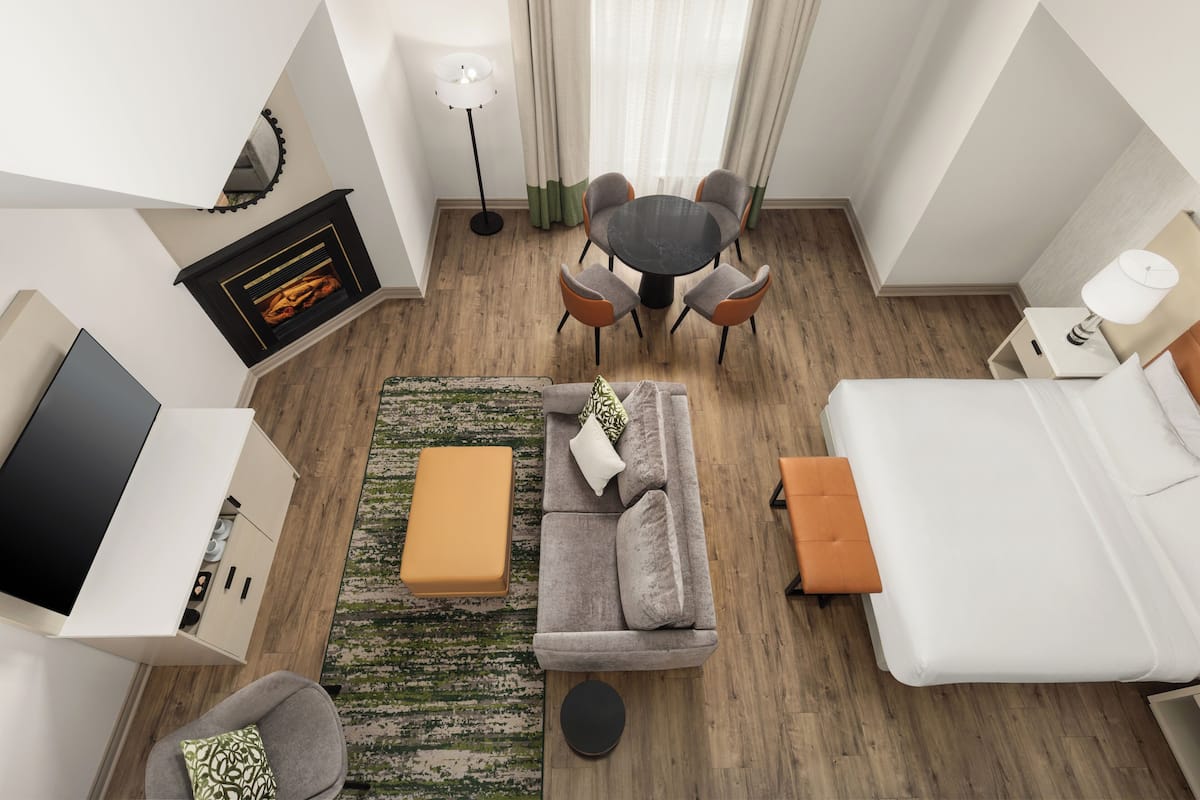 Une chambre d’hôtel moderne équipée d’un canapé, d’un pouf, d’une table à manger, de chaises et d’un téléviseur.