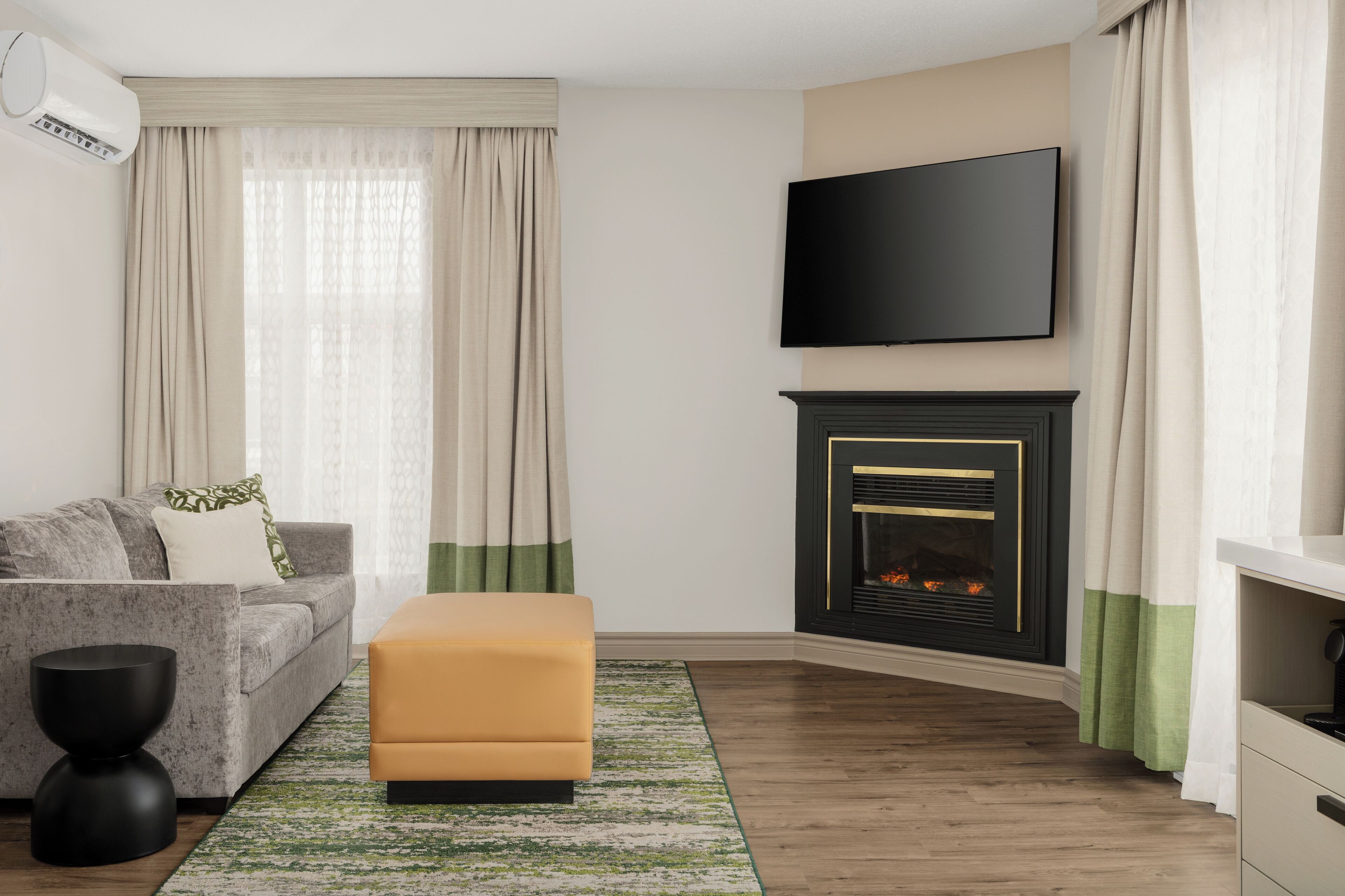 A modern living room with a sofa, ottoman, fireplace, TV, and curtains.