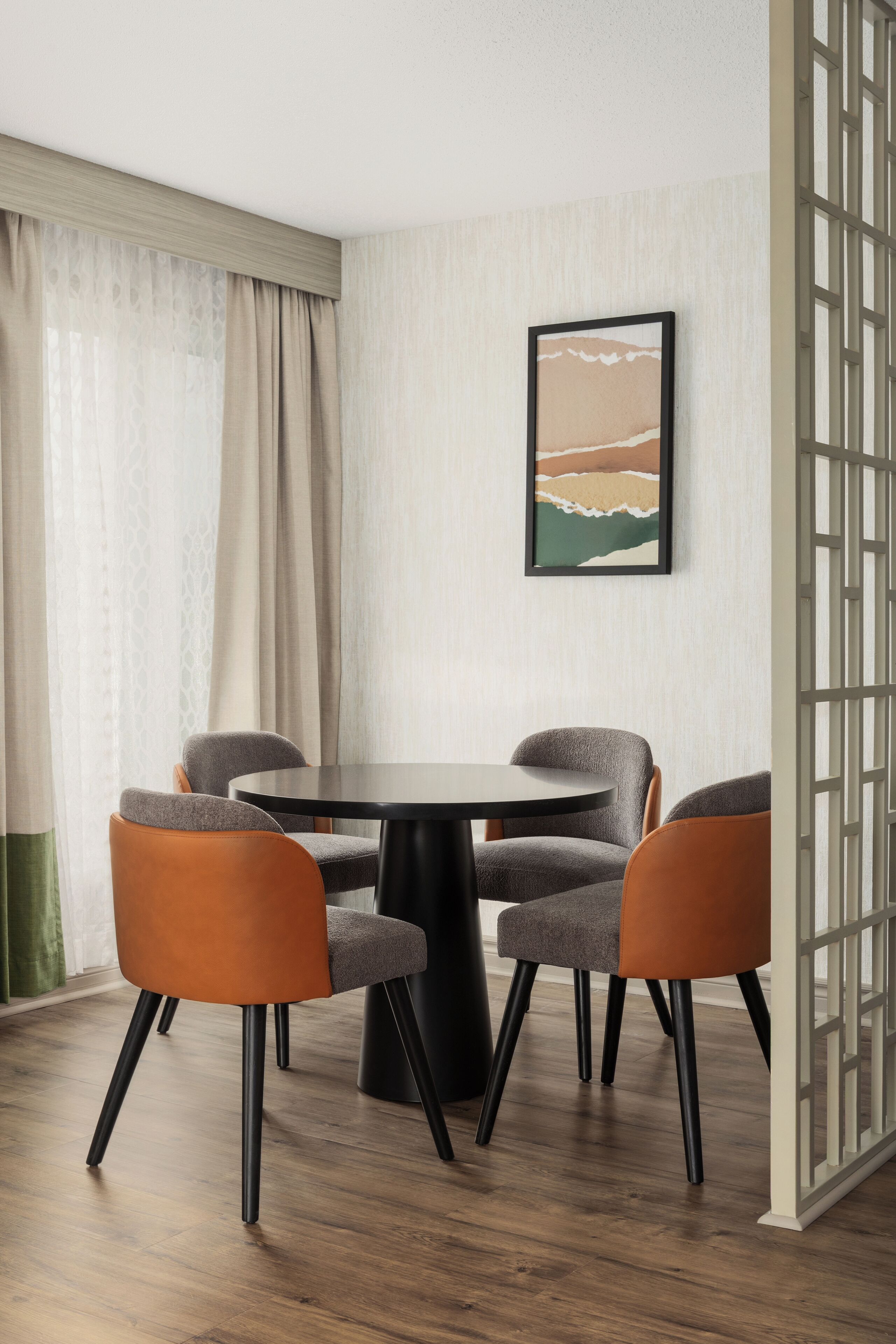 A dining area with a round table, four chairs, and a framed picture on the wall.