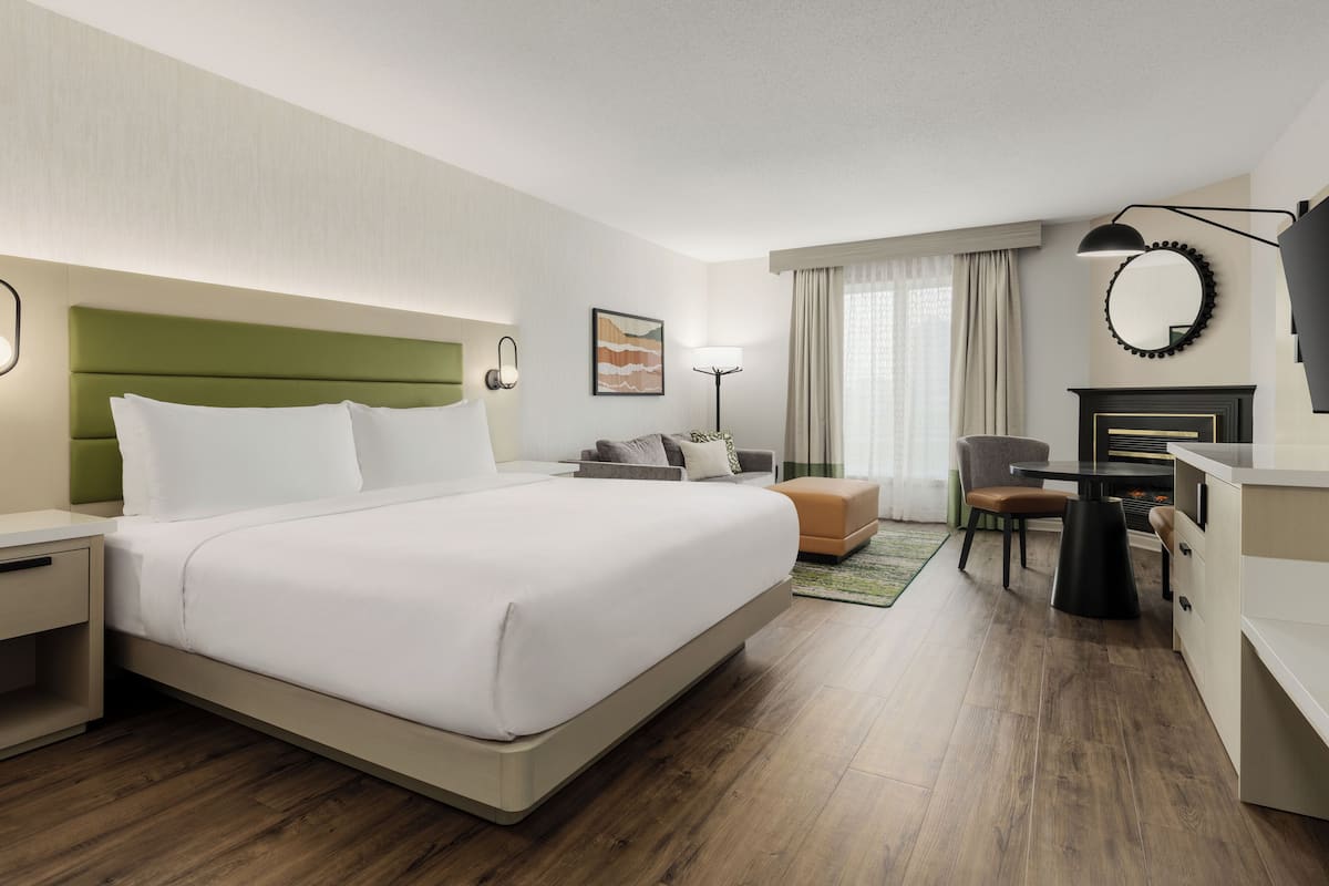 Une chambre d’hôtel avec un grand lit, un bureau, une chaise, une lampe et une cheminée.