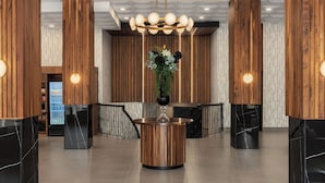 A lobby with a central reception desk, wooden paneling, a chandelier, and a refrigerator in the background. - Le Parc Gatineau, Tapestry Collection by Hilton (Gatineau)