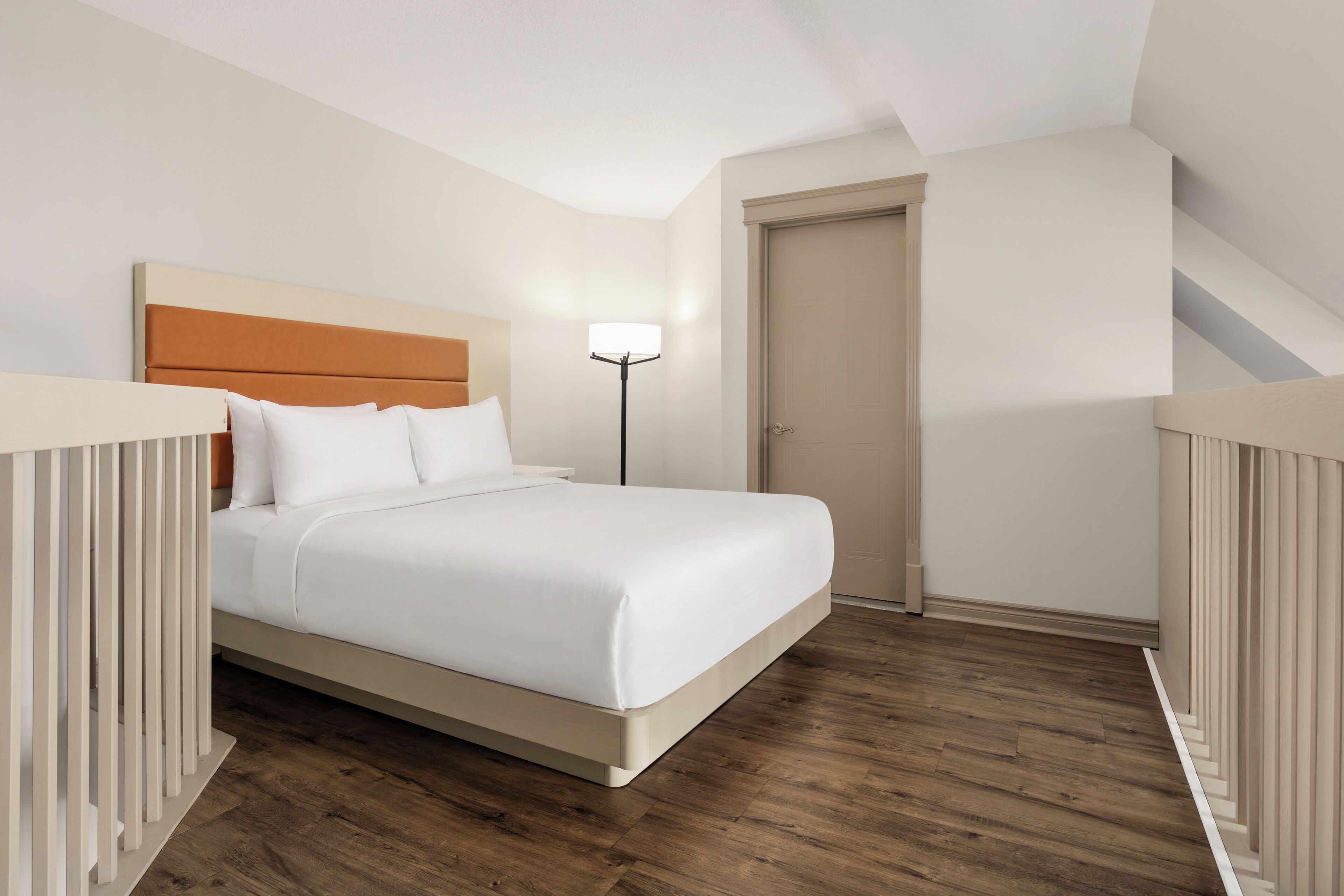 Une chambre d’hôtel avec un lit, une lampe de chevet, une porte et un escalier.