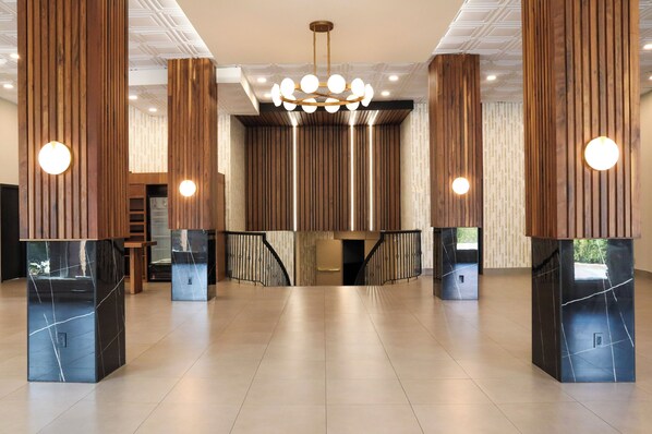 A spacious lobby with high wooden columns, a chandelier, and a staircase with black railings.
