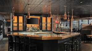 A bar area with a central island, bar stools, hanging copper pendant lights, and a brick wall backdrop. - Le Parc Gatineau, Tapestry Collection by Hilton (Gatineau)