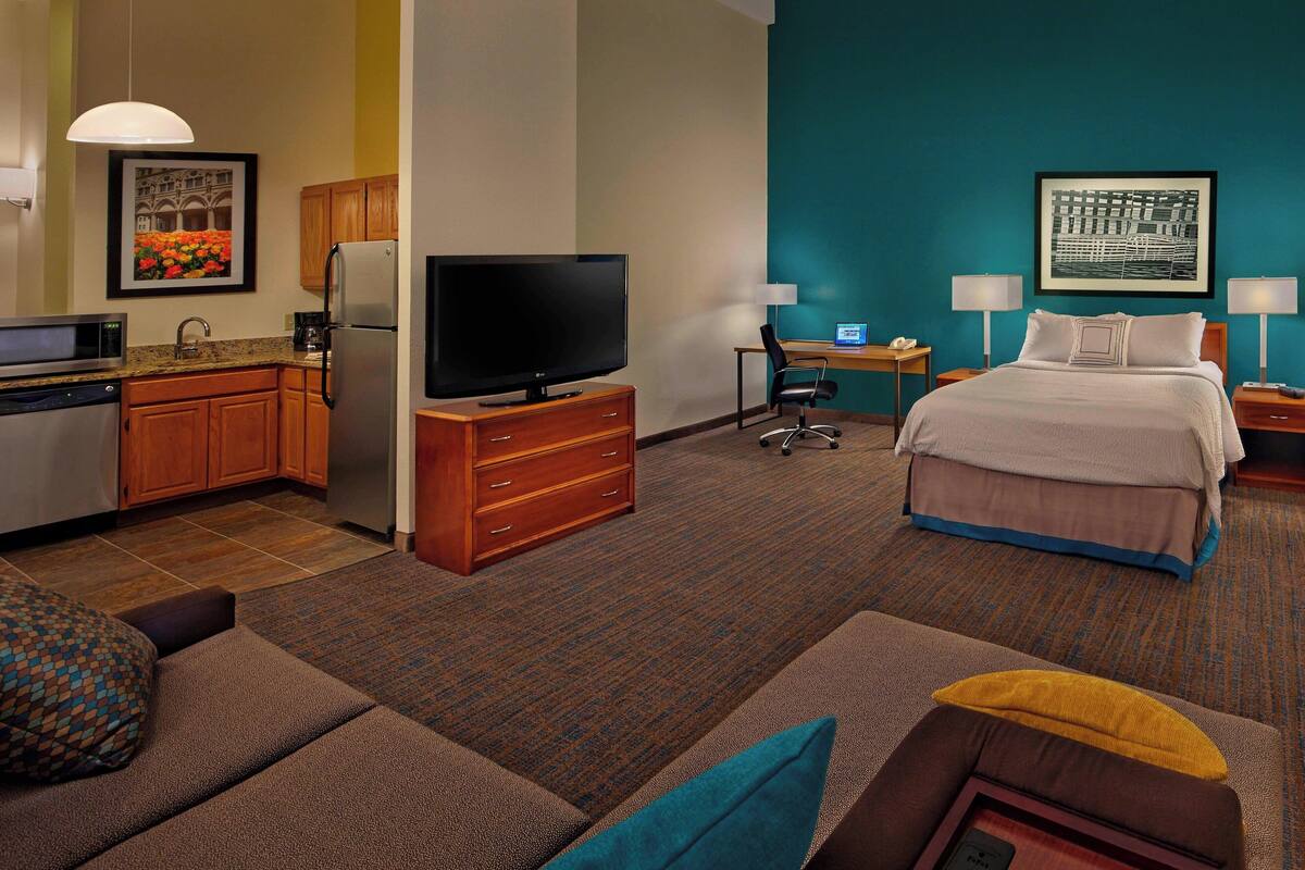 A hotel room with a kitchenette, a bed, a desk, and a TV.