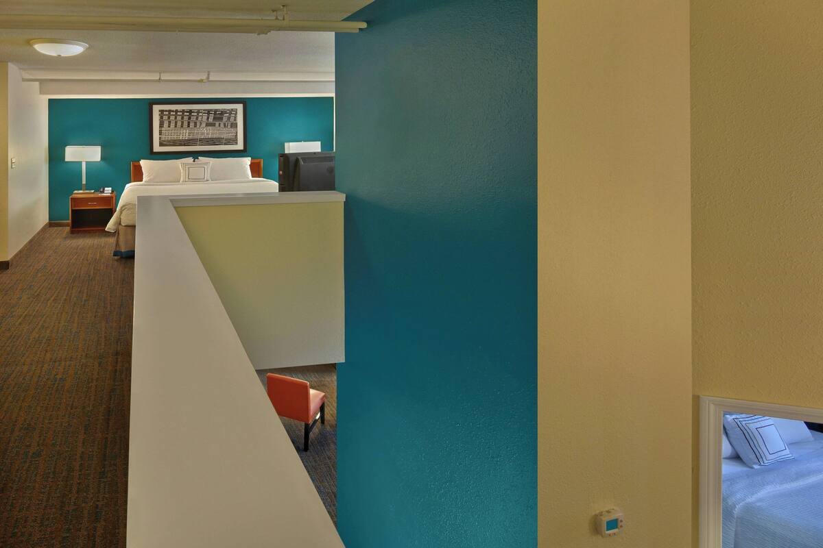 A hotel room with a bed, a desk, a chair, a nightstand, and a lamp.