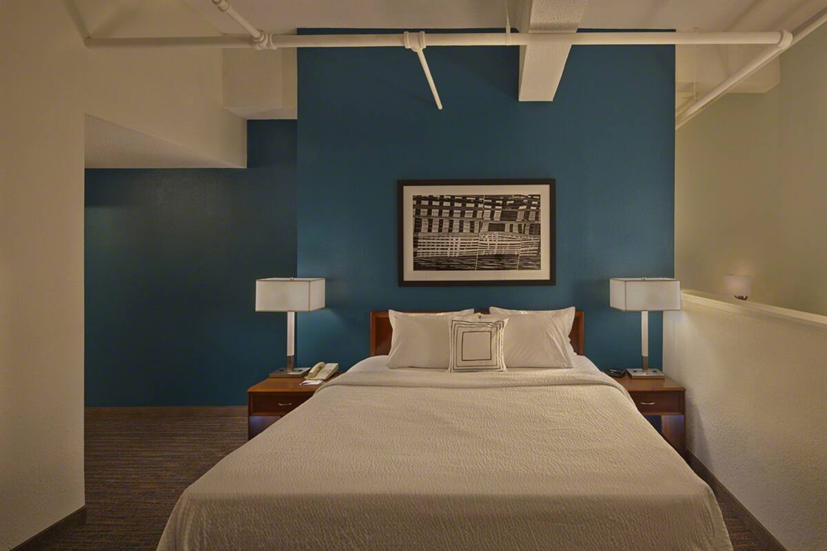 A hotel room with a large bed, two bedside tables with lamps, a framed artwork on the wall, and a blue accent wall.