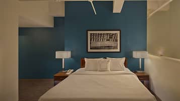 A hotel room with a large bed, two bedside tables with lamps, a framed artwork on the wall, and a blue accent wall.