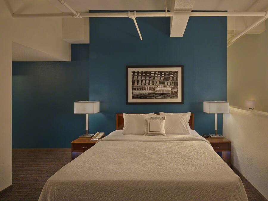 A hotel room with a large bed, two bedside tables with lamps, a framed artwork on the wall, and a blue accent wall.