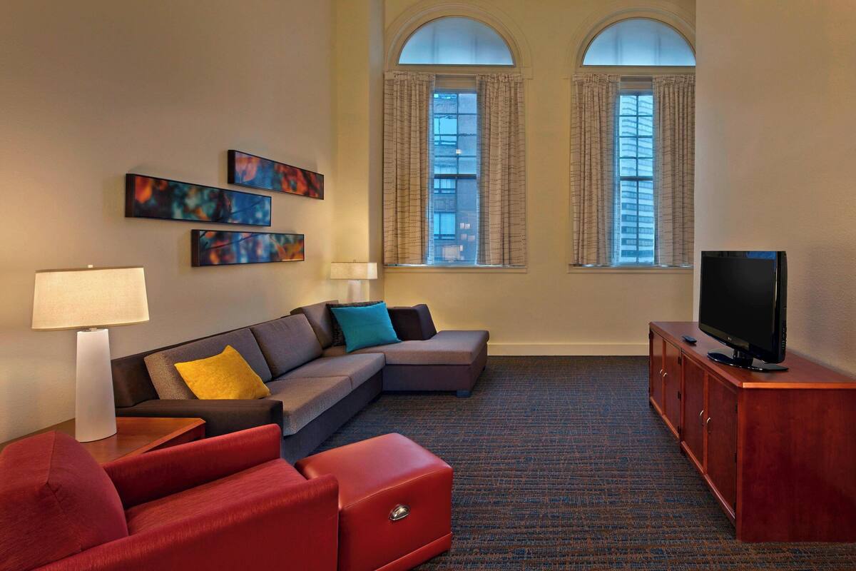 Una sala de estar moderna con un sofá seccional, un sillón rojo, un televisor sobre un mueble de madera y arte abstracto en la pared.