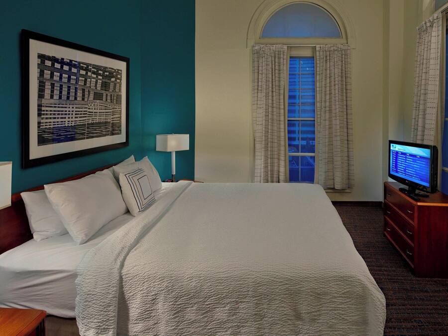 A hotel room with a large bed, a television on a wooden dresser, and a framed picture on the wall.