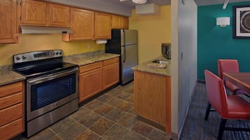A compact kitchen with wooden cabinets, a stainless steel oven, a refrigerator, and a microwave.