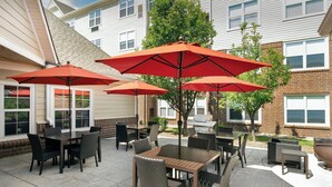 An outdoor patio with tables and chairs, surrounded by brick buildings and a tree. - Residence Inn By Marriott Denver Park Meadows (Englewood)