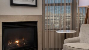 A fireplace with visible flames, a chair, a small round table, and a view through sheer curtains. - Residence Inn By Marriott Denver Park Meadows (Englewood)