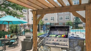 Ein Grillbereich im Freien mit Steinmauern, einer Holzhütte und einem Pool im Hintergrund.