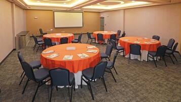 Une salle de conférence dotée de plusieurs tables rondes, chacune recouverte d’une nappe blanche et entourée de chaises.
