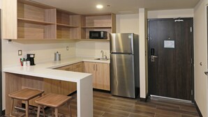 A modern kitchen with wooden cabinets, a stainless steel refrigerator, a microwave, and a sink. There are two wooden stools at the counter. - Holiday Inn Ciudad Juarez by IHG (Ciudad Juárez)