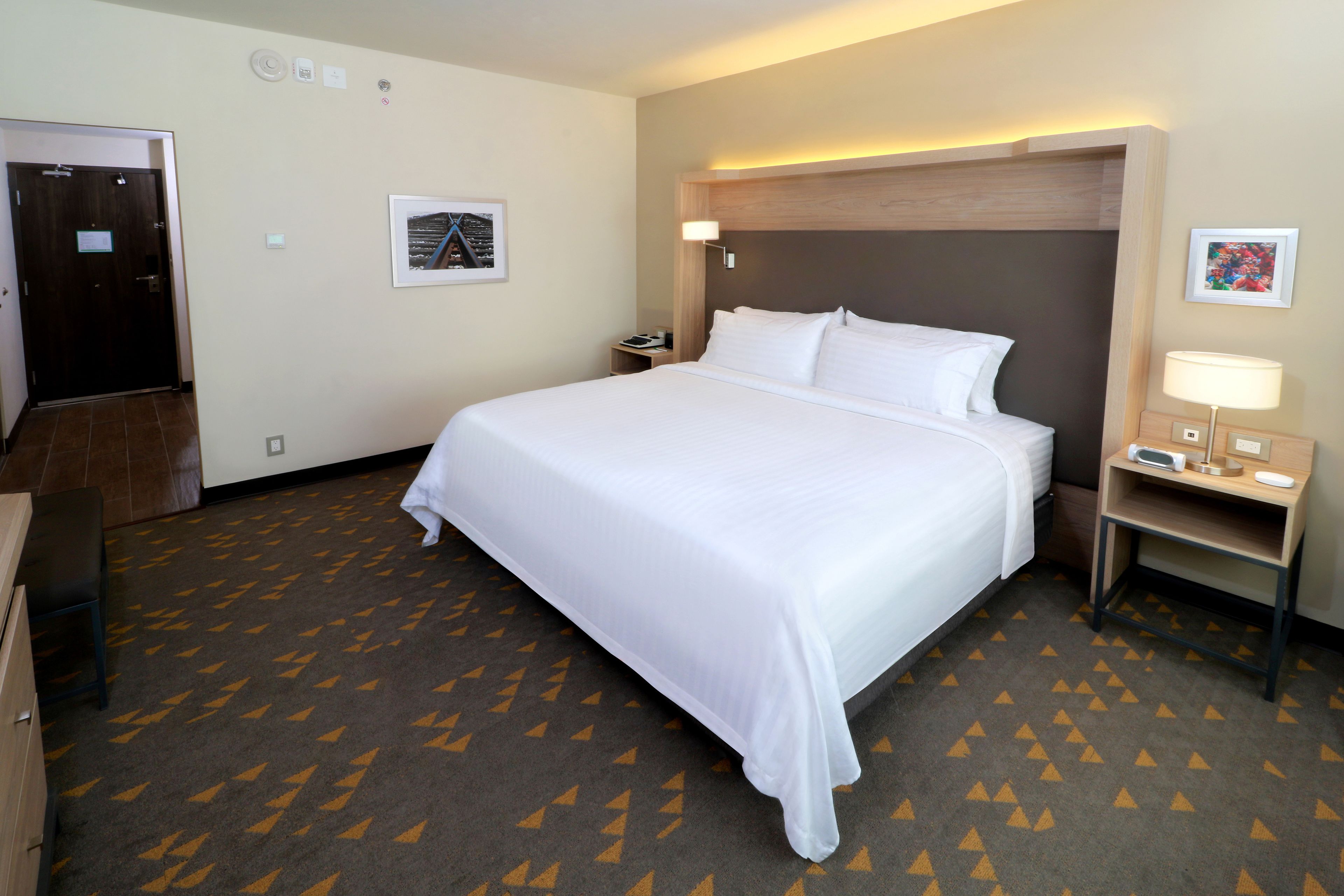 A hotel room with a large bed, a bedside table with a lamp, a nightstand, and a door.