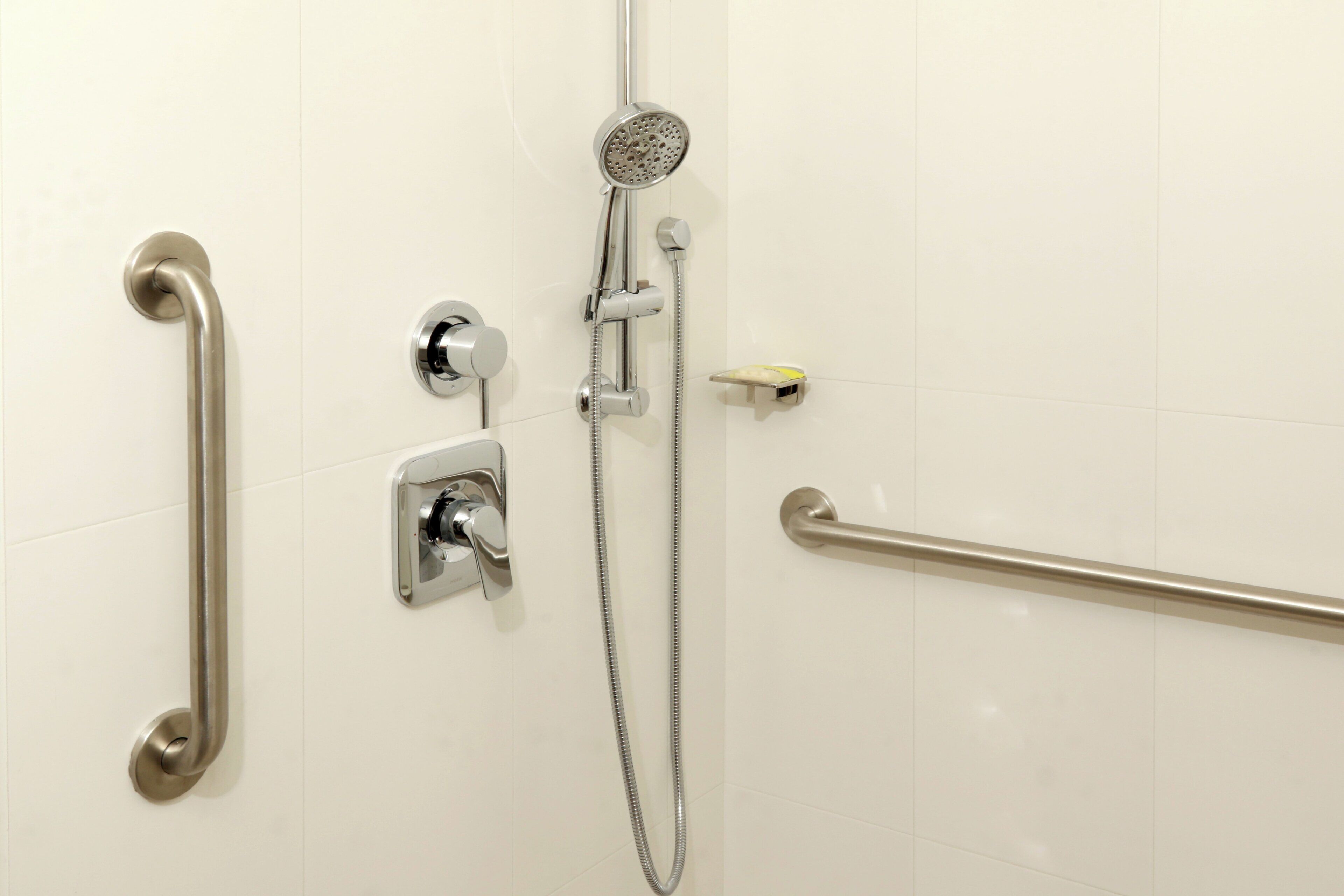 Un espace douche équipé d’un pommeau de douche à main, d’un flexible de douche et d’une barre d’appui.