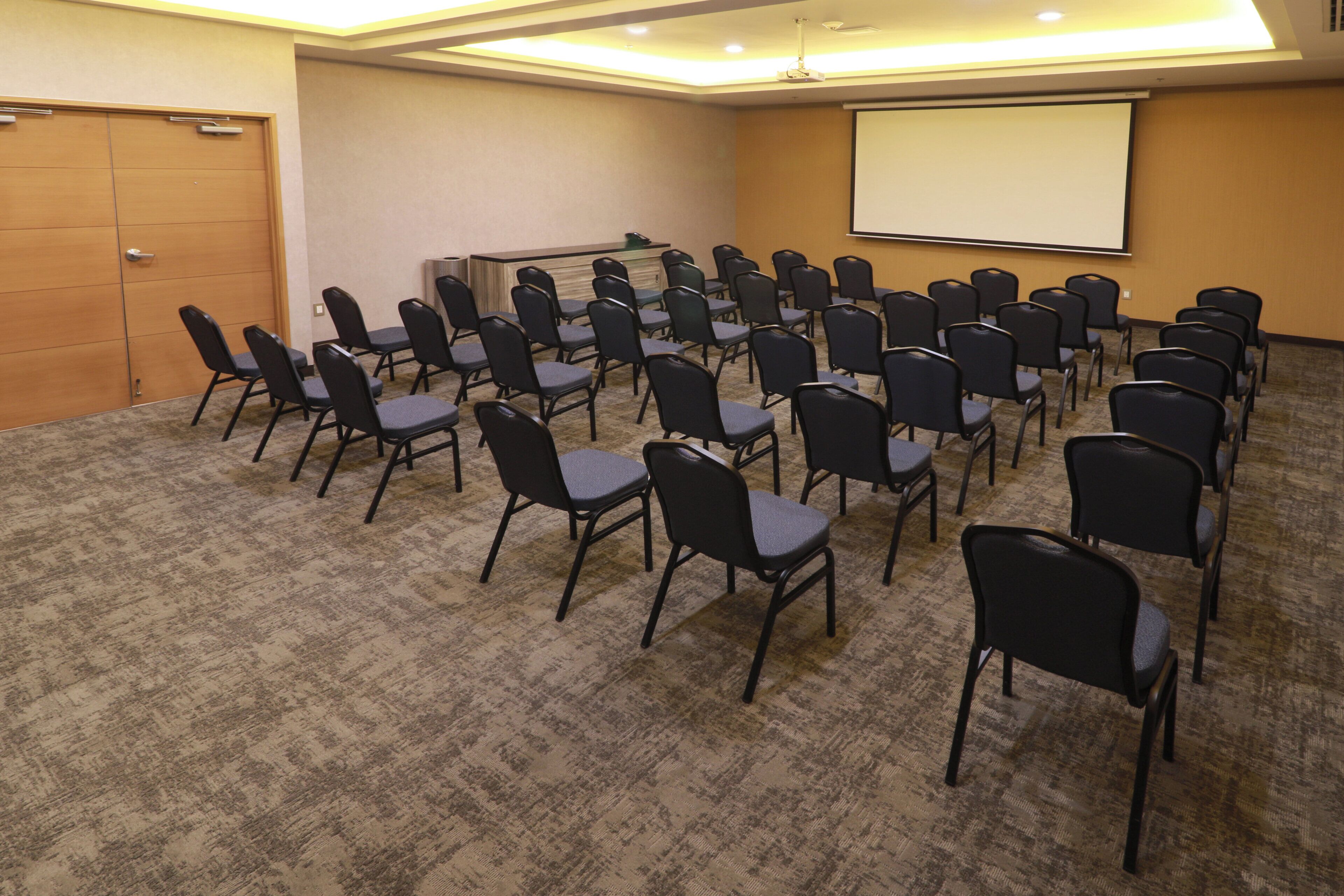 A conference room with rows of chairs facing a projection screen, a podium, and a door.