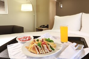 A hotel room with a bed, a bedside table with a lamp, a tray with breakfast including a sandwich, fries, and a glass of orange juice. - Holiday Inn Ciudad Juarez by IHG (Ciudad Juárez)