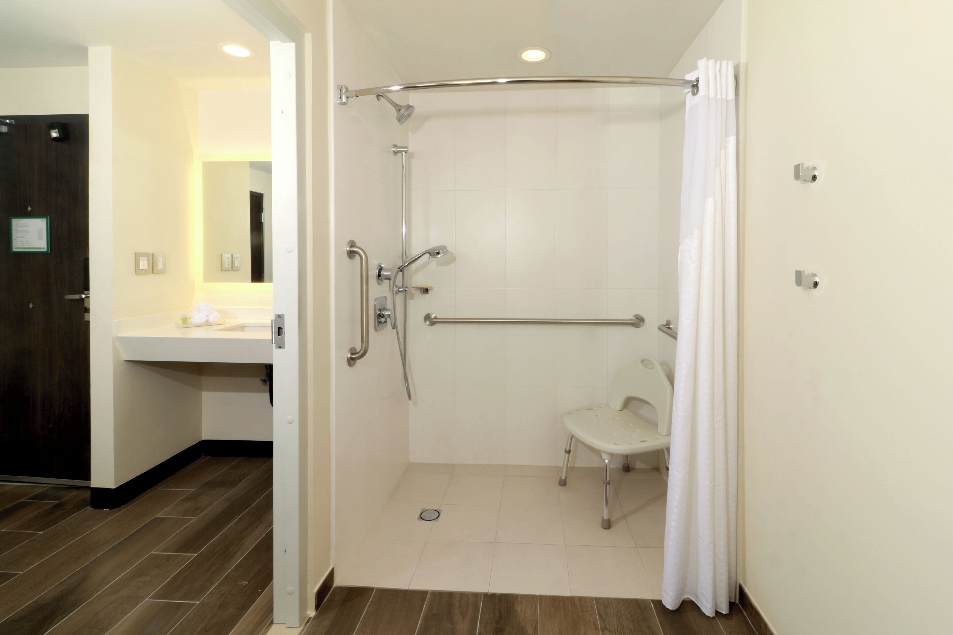 Un baño moderno con ducha, barra de apoyo, inodoro y lavamanos.