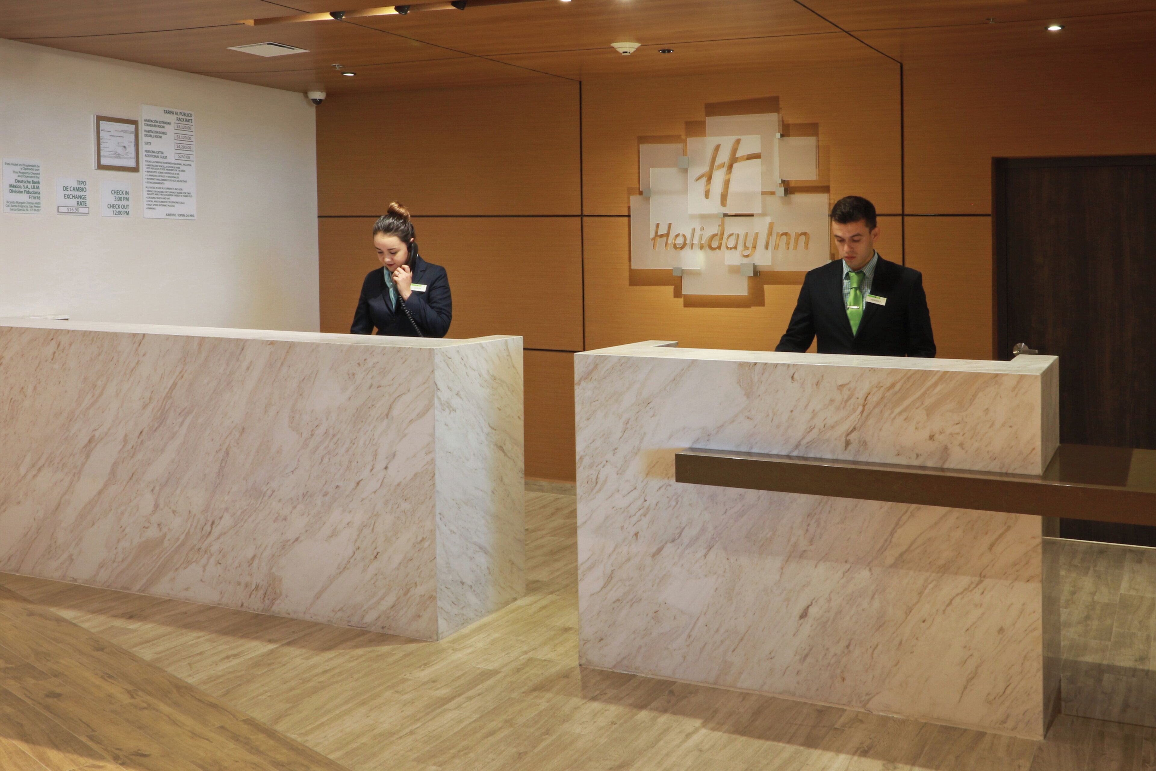 A reception desk with a Holiday Inn sign, a wooden floor, and a wall with a bulletin board.