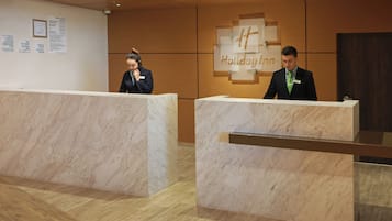 A reception desk with a Holiday Inn sign, a wooden floor, and a wall with a bulletin board.