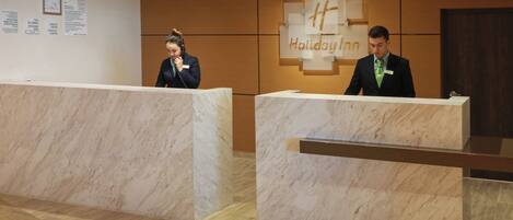 A reception desk with a Holiday Inn sign, a wooden floor, and a wall with a bulletin board.