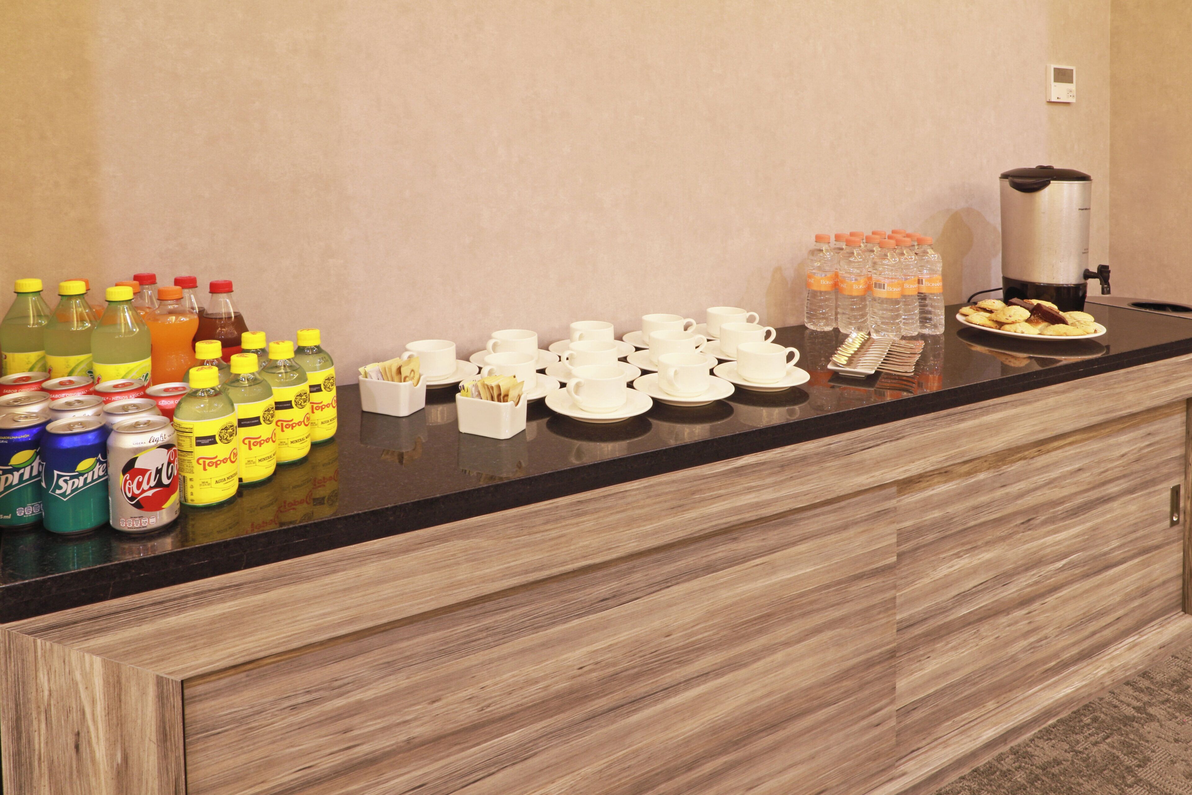 Disposição de buffet de café da manhã com diversas bebidas, xícaras e uma cafeteira.