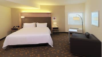A hotel room with a large bed, bedside tables, a desk, a chair, a window, and a wall-mounted lamp.