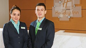 Two individuals standing in front of a wooden reception desk with a sign that reads "Holiday Inn." - Holiday Inn Ciudad Juarez by IHG (Ciudad Juárez)