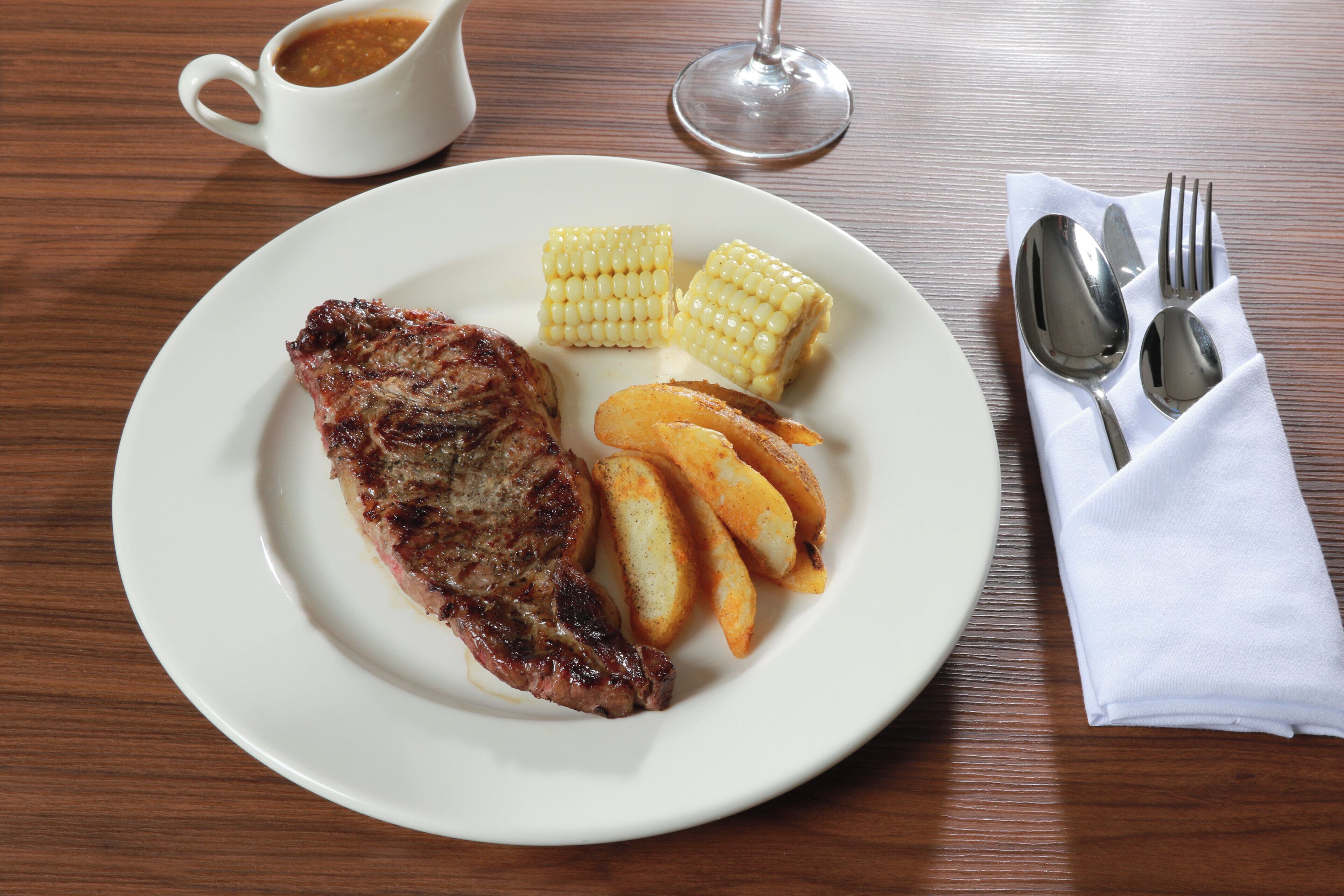 Un plato con un bistec, mazorca de maíz y papas asadas.