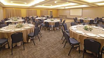 Un salón de conferencias con mesas redondas, sillas y una pantalla para proyector.