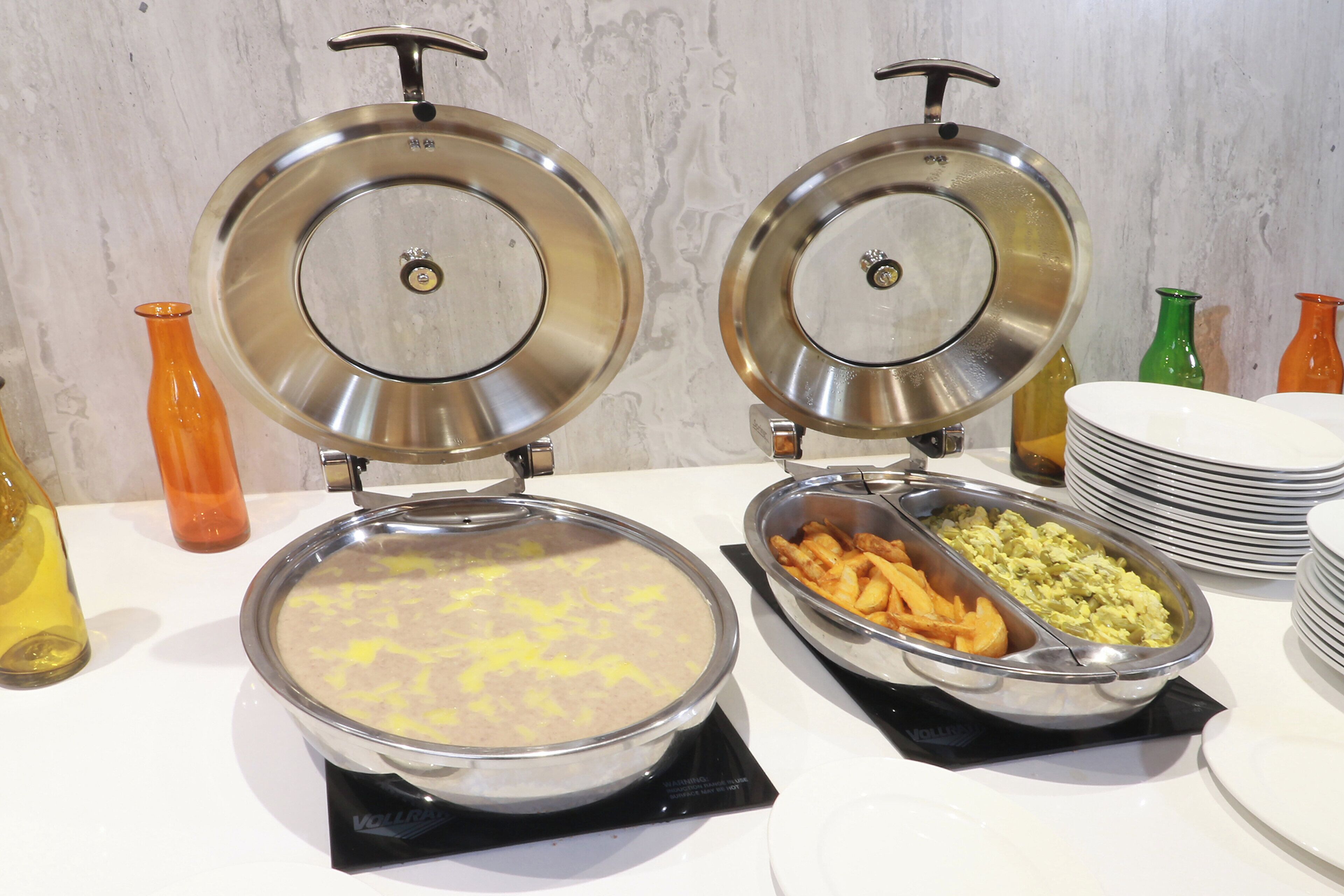 A buffet setup with two covered food dispensers and a variety of dishes including potatoes and vegetables.