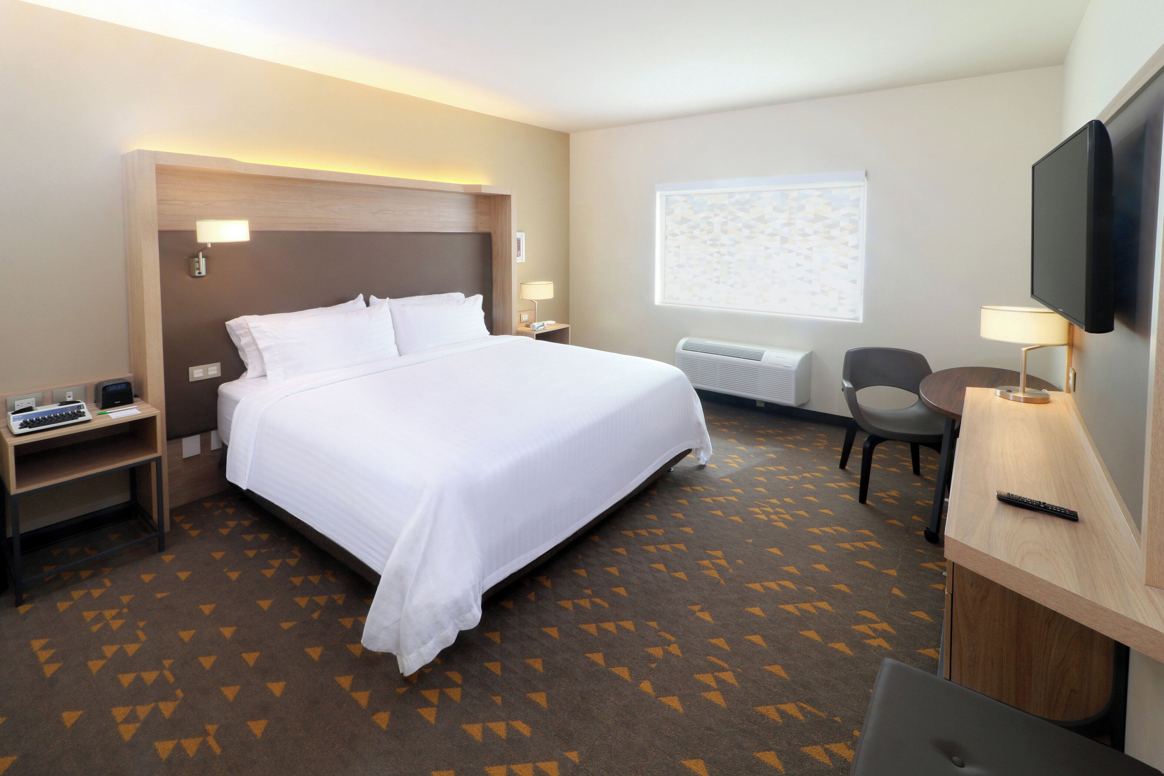 A hotel room with a bed, a desk, a chair, a television, and a window with blinds.