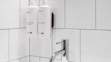 Un baño moderno con azulejos blancos, un grifo cromado y dos botellas de jabón para manos y cuerpo.