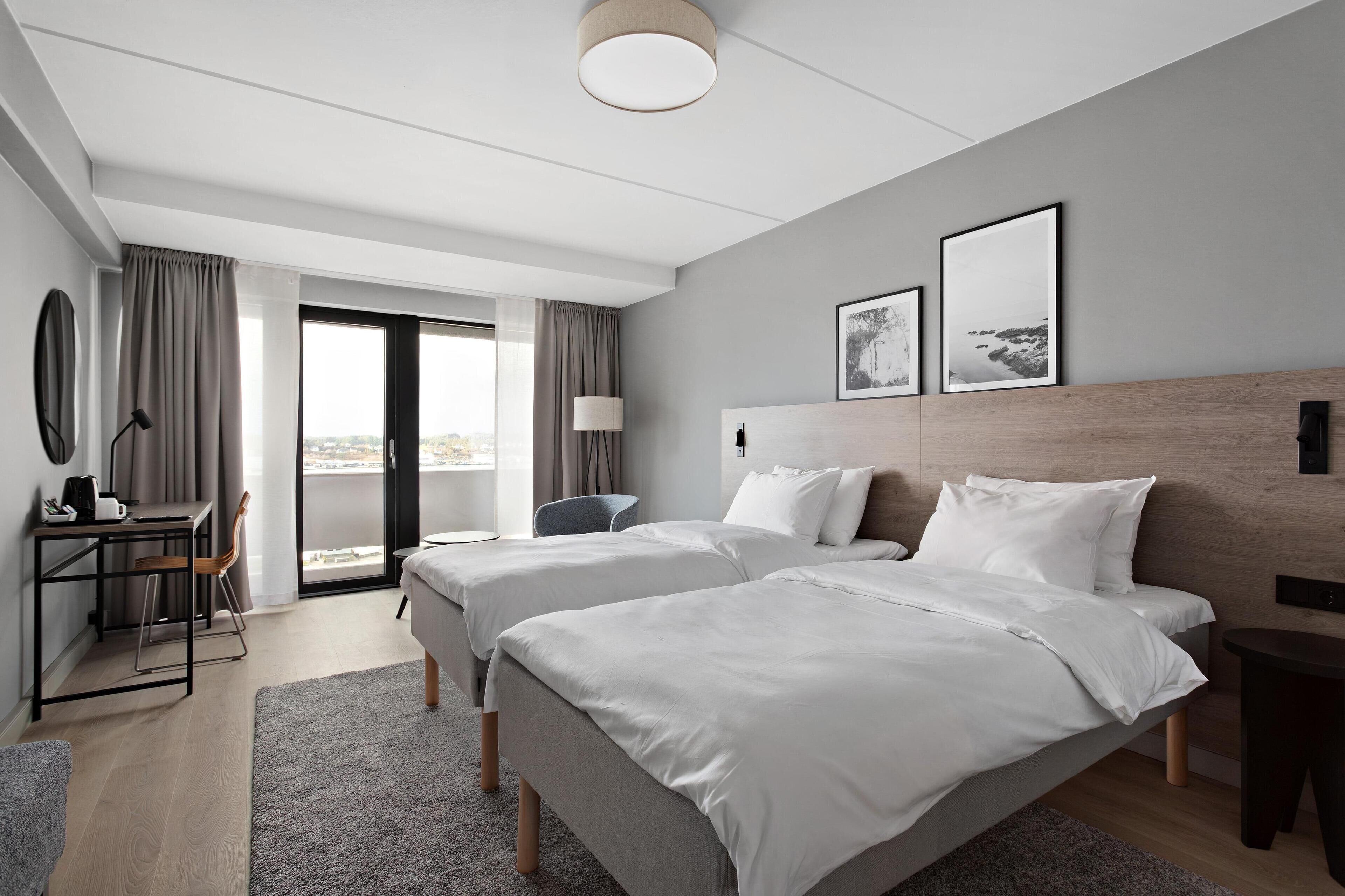 A modern hotel room with two beds, a desk, and a chair.