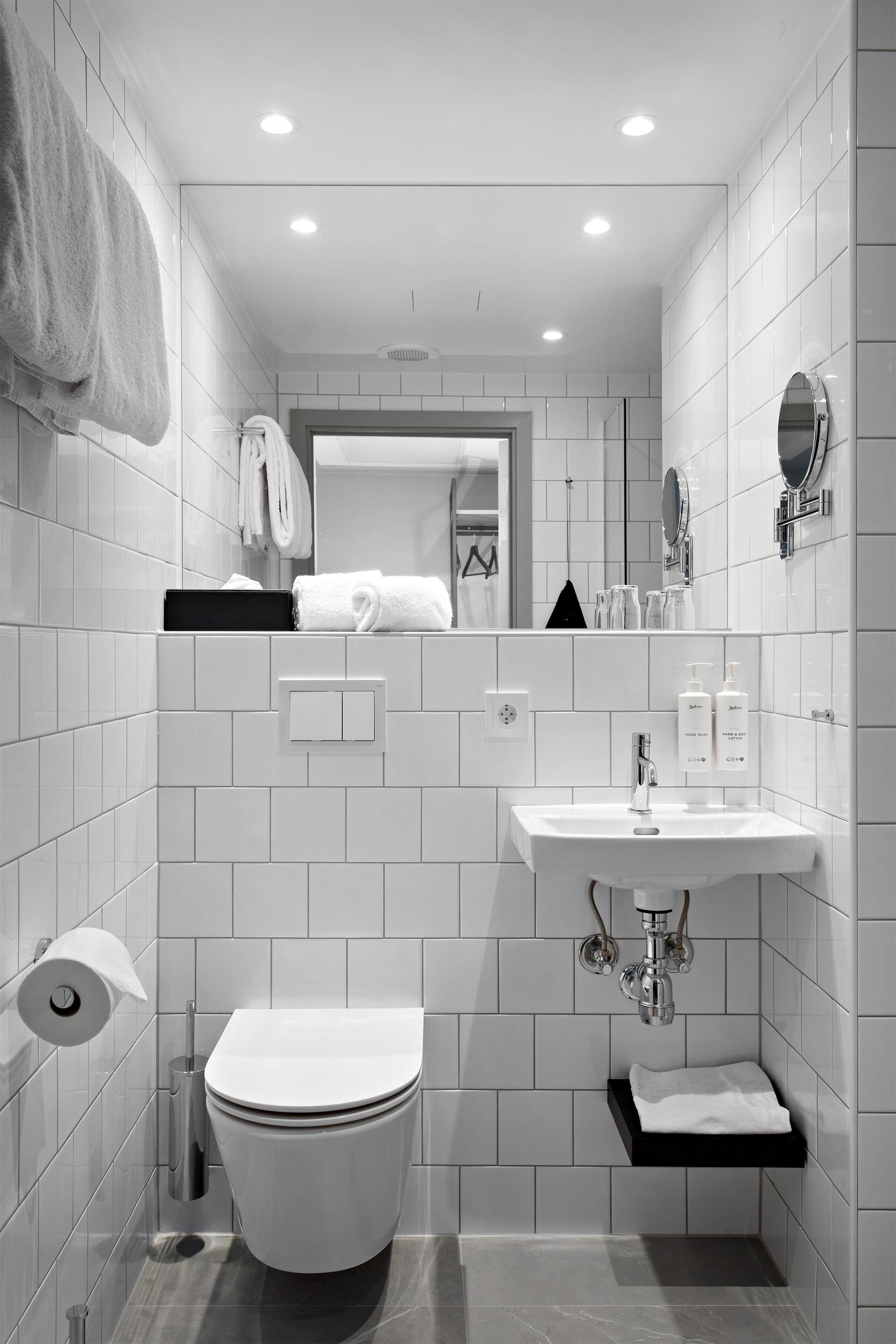 A modern bathroom with white tiles, a toilet, a sink, and a mirror.