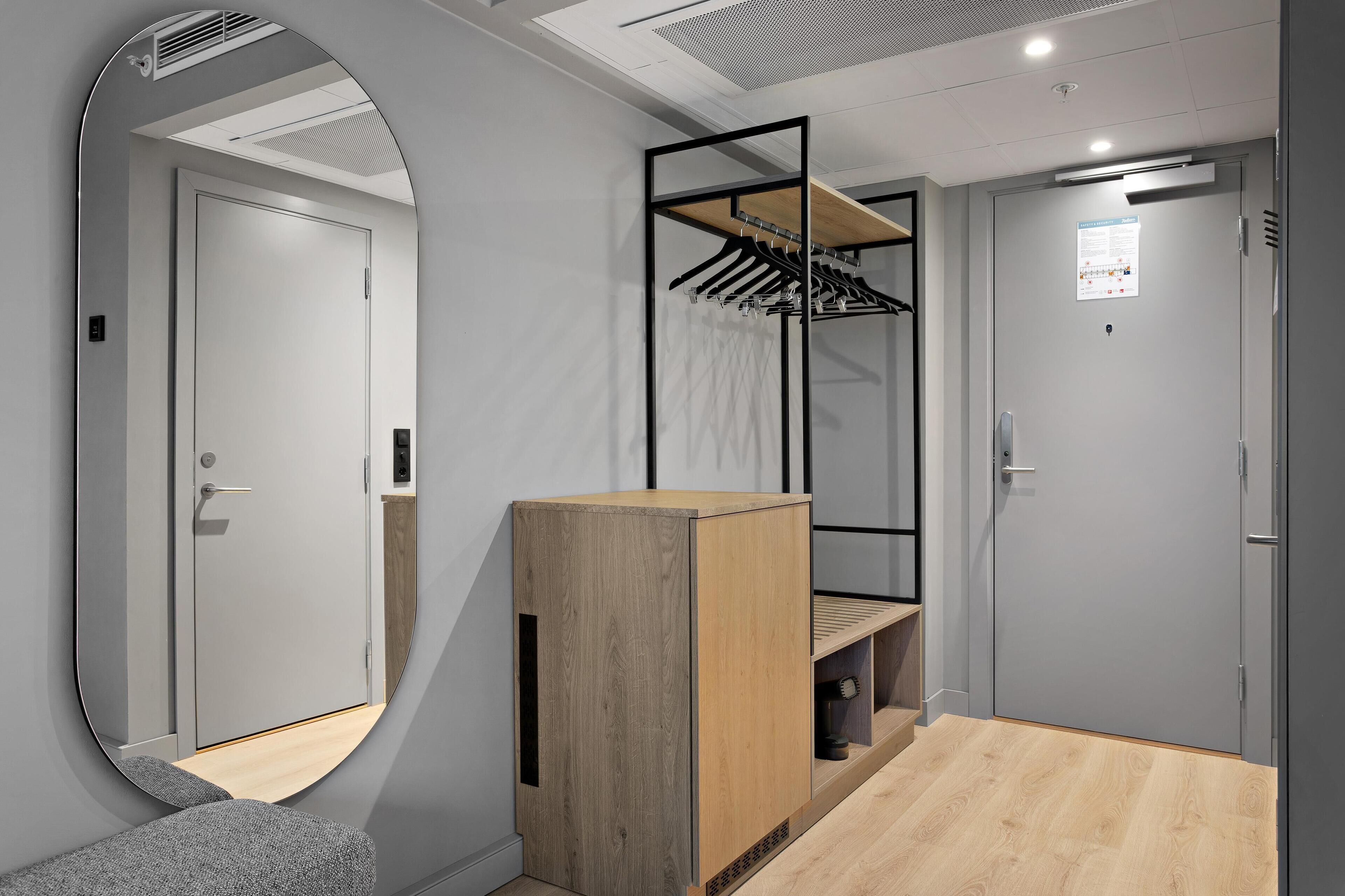 A modern hotel room with a wooden cabinet, a mirror, and a built-in wardrobe with a hanging rack.