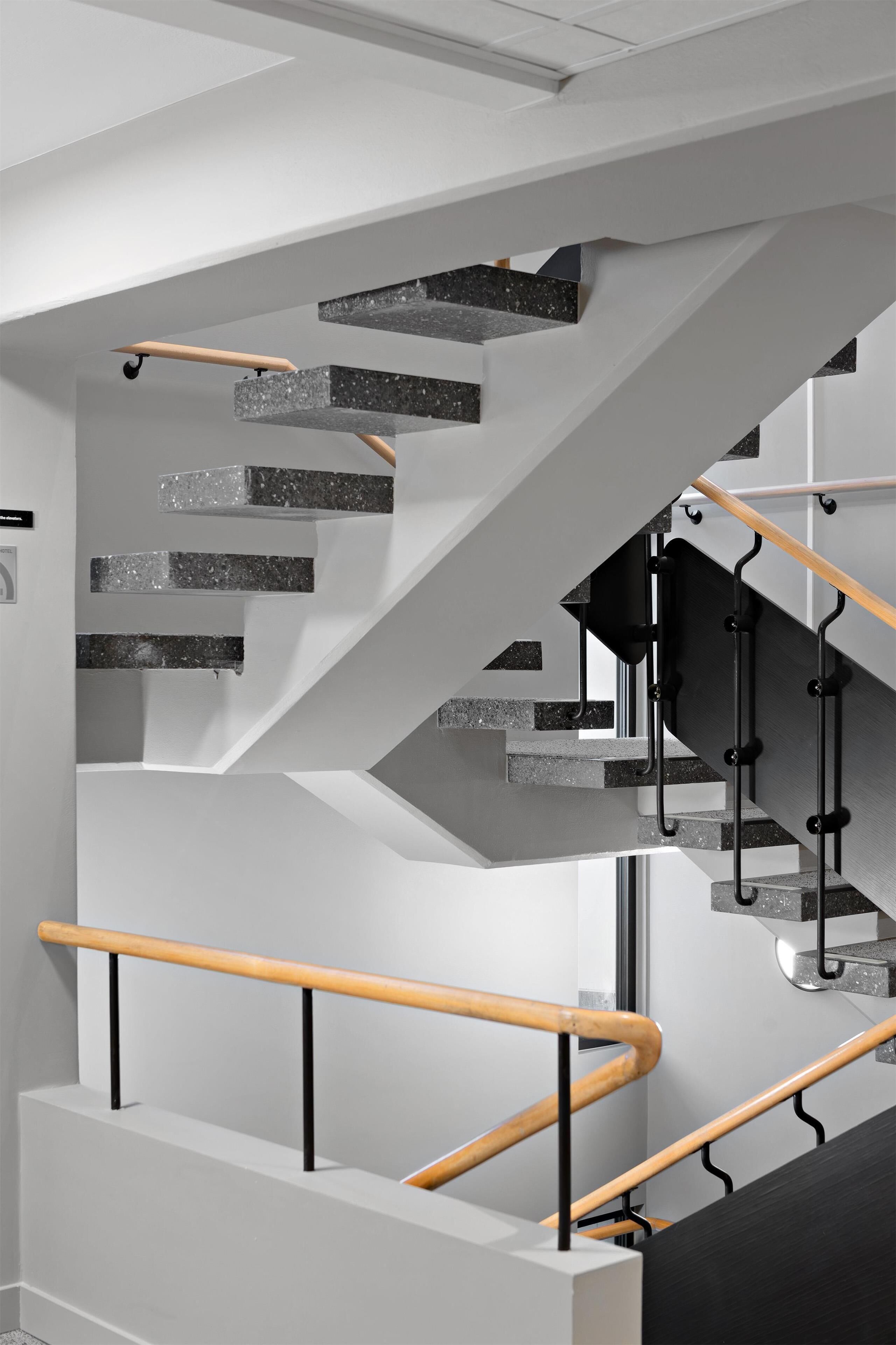 Un escalier moderne au design géométrique, avec des rampes en métal et une combinaison de béton et de bois.