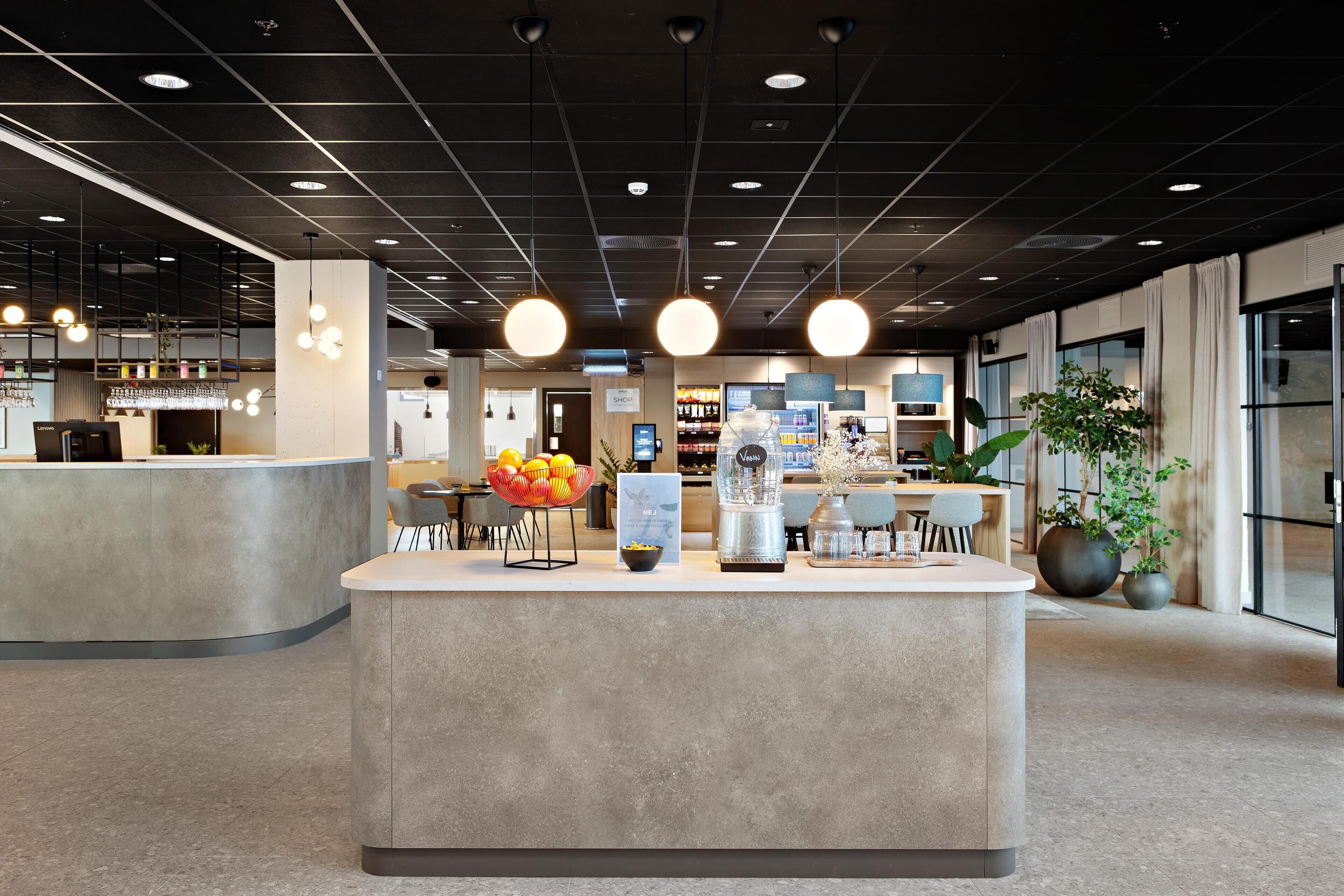A modern reception area with a central counter, seating, and a variety of amenities including a coffee machine and decorative plants.