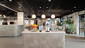 Een moderne receptie met een centraal loket, zitplaatsen en diverse voorzieningen, waaronder een koffieapparaat en decoratieve planten.