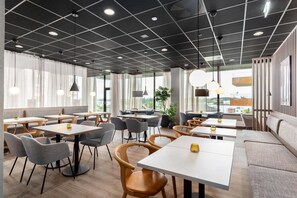 A modern dining area with tables and chairs, large windows, and a view of the city.