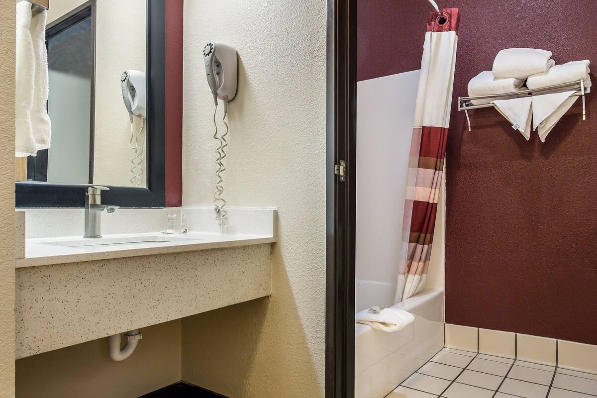 Ein Badezimmer mit Waschbecken, Spiegel, Fön und Handtuchhalter mit Handtüchern.