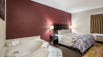 A hotel room with a large bed, a separate bathroom with a bathtub, and a bedside table with a lamp.