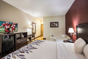 A hotel room with a bed, a desk, a television, a bathroom, and a door.
