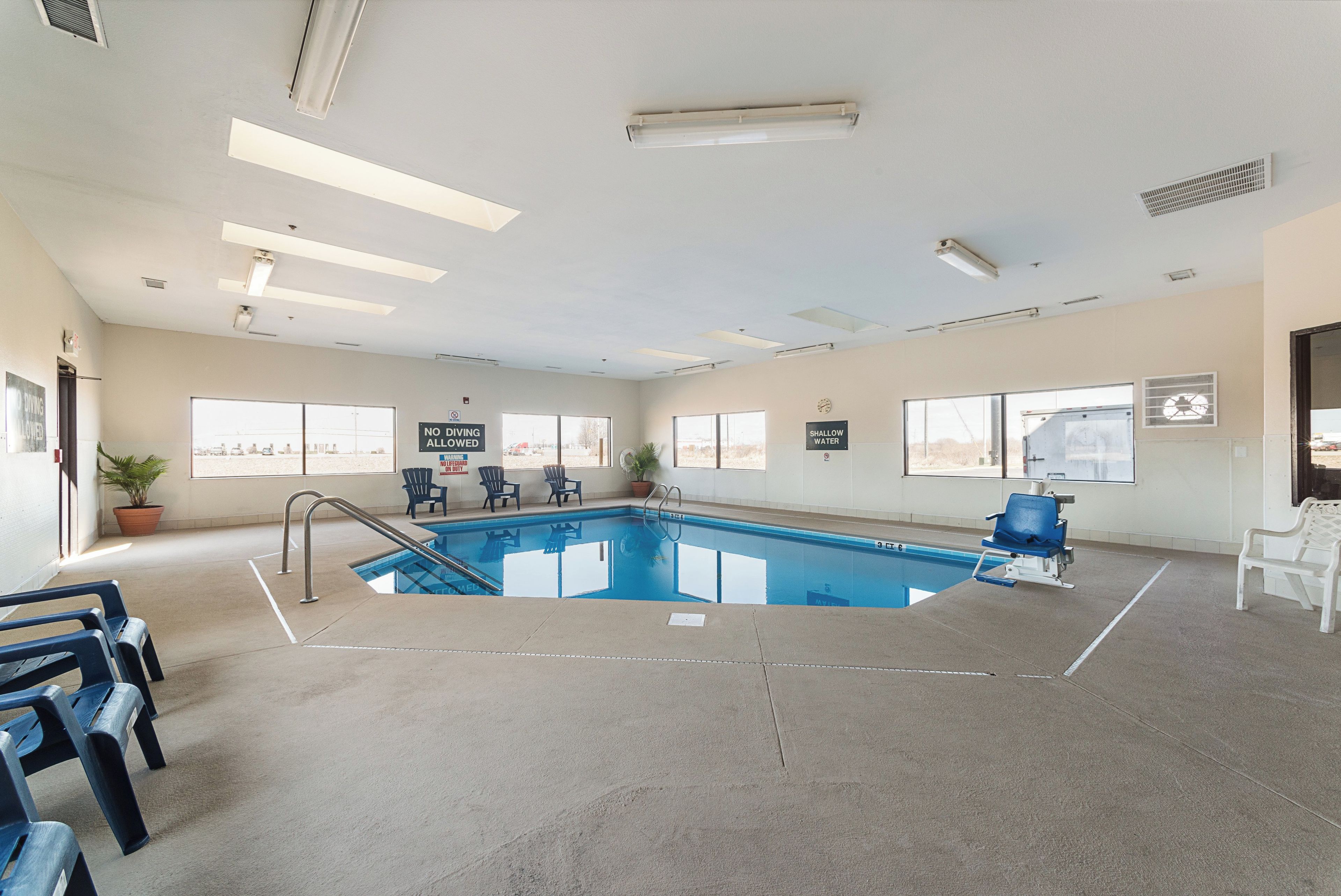 Una piscina interior con señalización clara, una silla de salvavidas y vistas al exterior a través de amplias ventanas.